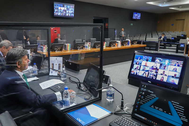 Foto no Plenário do CNJ mostra o presidente Fux olhando para um telão à sua frente onde estão as pessoas participantes da reunião por videoconferência.
