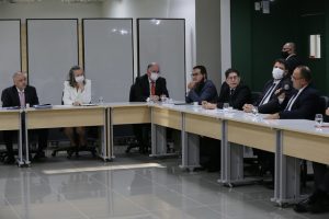 Foto mostra pessoas em uma sala sentadas em volta de uma mesa em U.