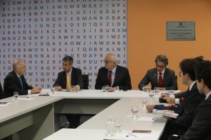 Foto mostra momento da reunião, com as pessoas sentadas em volta de uma mesa em U.