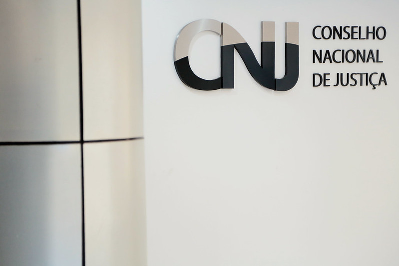 Foto de logomarca do CNJ em uma parede branca.
