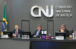 Foto mostra, sentados na bancada principal do Plenário do CNJ durante a cerimônia, da esquerda para a direita, o procurador-geral da Justiça Militar, Antônio Pereira Duarte; o presidente do CNJ, ministro Luiz Fux; e o secretário-geral do CNJ, Valter Shuenquener.