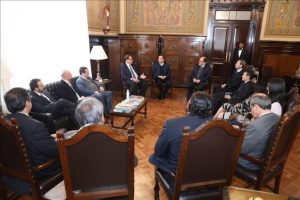 Foto mostra pessoas sentadas em uma sala e conversando.