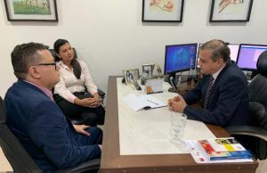 dois homens e uma mulher em reunião envolta de uma mesa