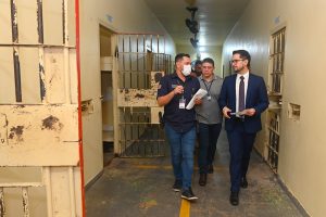 homens caminhando entre celas de presídio