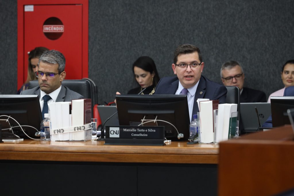 Fotografia em plano médio, ao centro os conselheiros do Conselho Nacional de Justiça, Marcello Terto e João Paulo Schoucair, sentados e vestidos formalmente.