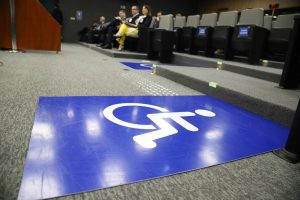 Imagem da placa de sinalização visual para pessoas com deficiência física. Placa de tom azul e ícone de um cadeirante.