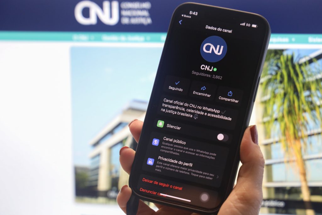 Imagem em plano detalhe; em destaque um aparelho celular, na tela estão explícitos dados do perfil do canal oficial do CNJ no WhatsApp.