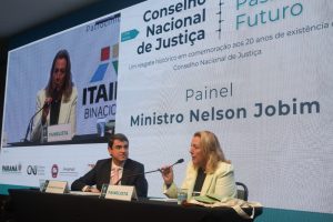 Fotografia em plano médio do conselheiro Bandeira de Mello e a ex - conselheira Ruth Scholte de Carvalho, durante a abertura do evento comemorativo de 20 anos do CNJ. Ao fundo painel referente ao evento com o texto: Conselho Nacional de Justiça - Presente, Passado e Futuro - Um resgate histórico em comemoração aos 20 anos de existência do Conselho Nacional de Justiça - Painel - Ministro Nelson Jobim.