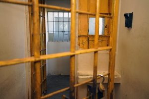 Fotografia de uma cela do complexo prisional de Aparecida de Goiânia. Sala com paredes em tom de amarelo claro, composta por grades, balcão e interfone.