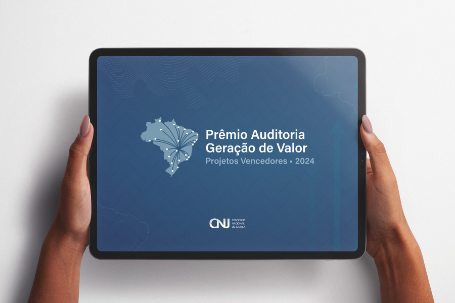 Duas mãos seguram um tablet que transmite um card azul com a imagem do mapa do Brasil e a inscrição “Prêmio Auditória Geração de Valor” e “Projetos Vencedores 2024”. Na parte inferior, o logotipo do Conselho Nacional de Justiça (CNJ) na parede, juntamente com a inscrição “Conselho Nacional de Justiça”.